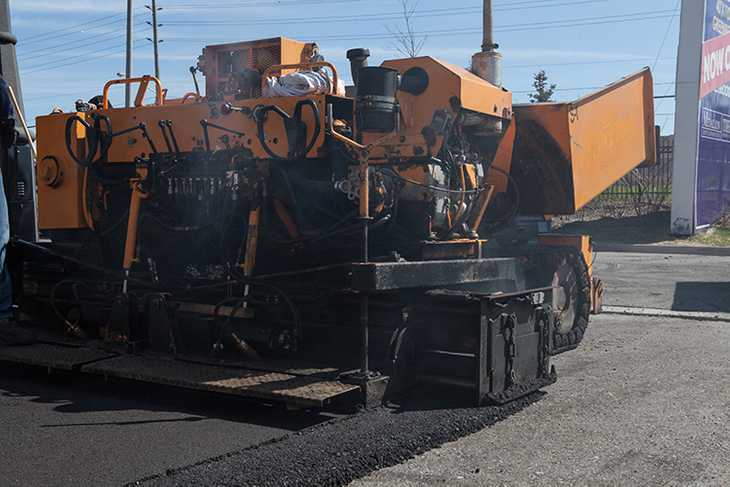 A large paving vehicle adding pavement to a commercial driveway.
